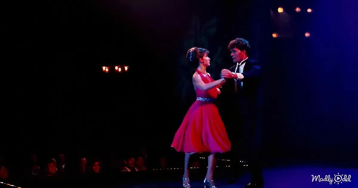 A couple in formal attire dances elegantly on stage under dim lighting.