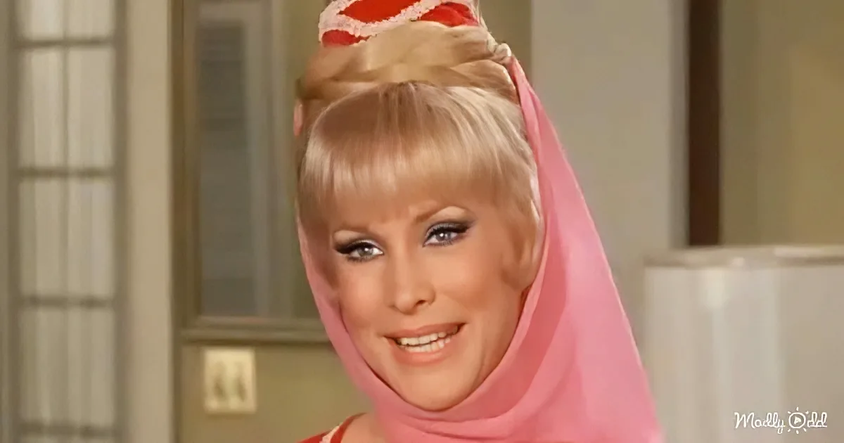 A woman with blonde hair styled in a bun, wearing a pink headscarf and a red outfit, smiles warmly.