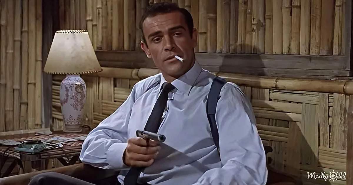 A man in a white shirt and suspenders holds a gun, smokes a cigarette, and sits in a bamboo-walled room.