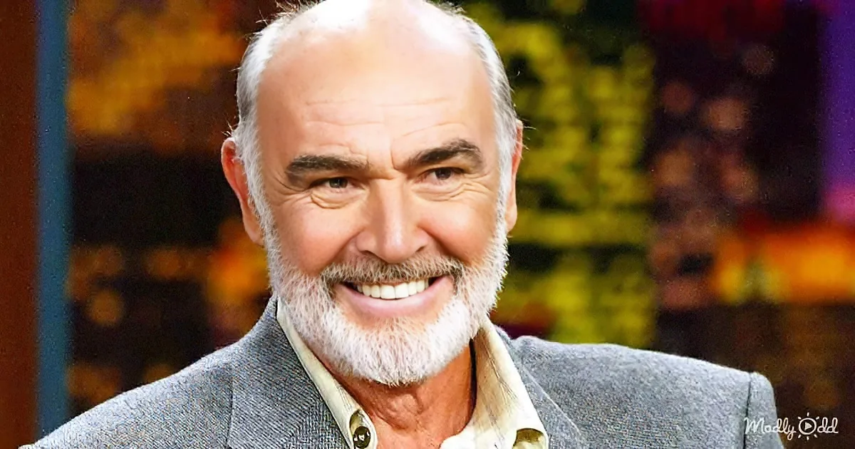 A smiling man with a white beard and gray suit jacket, set against a blurred background.