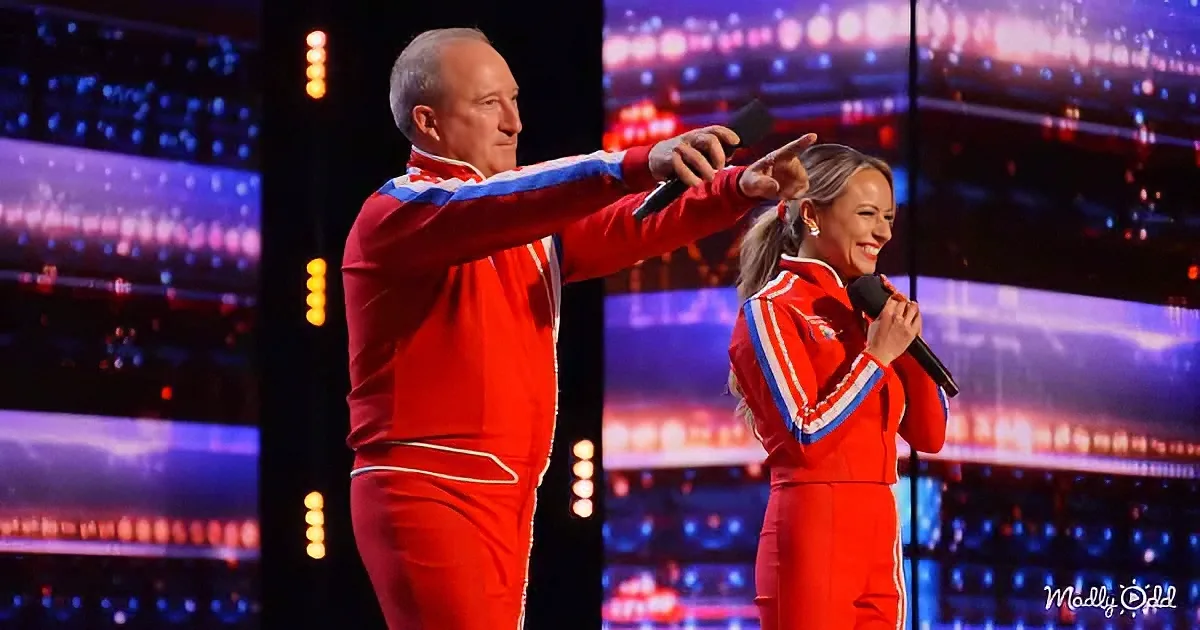A man in a red tracksuit points while a woman in a red tracksuit holds a microphone on stage.