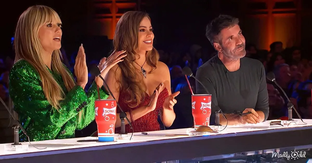 Three judges, one clapping, one pointing, one listening, seated at a table with microphones and drinks.