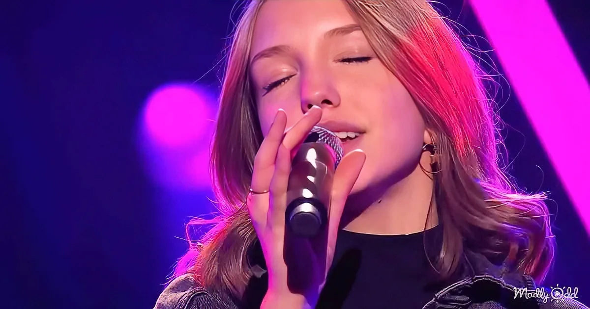 A person singing passionately into a microphone, illuminated by purple stage lights.