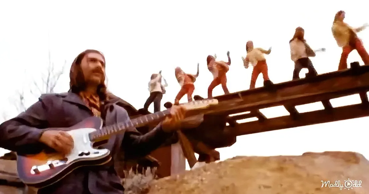 A man plays guitar while a group of people dance on a bridge in the background.