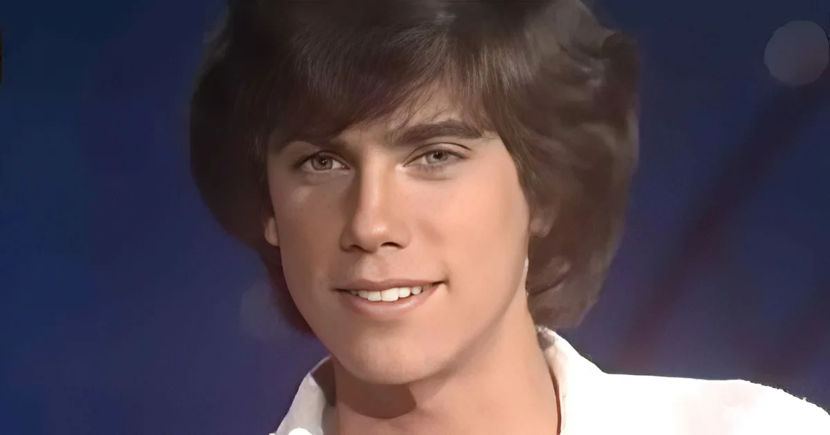A smiling young man with short, dark hair and a white shirt against a dark blue background.