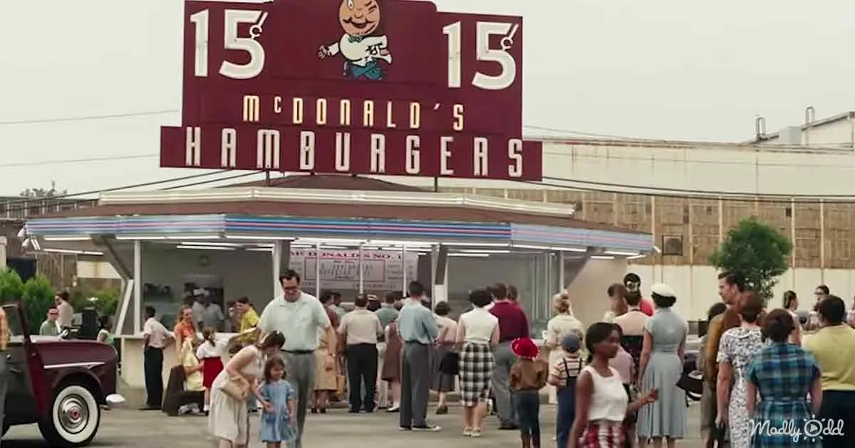 People queue outside a vintage McDonald's restaurant with a sign advertising hamburgers for 15 cents.