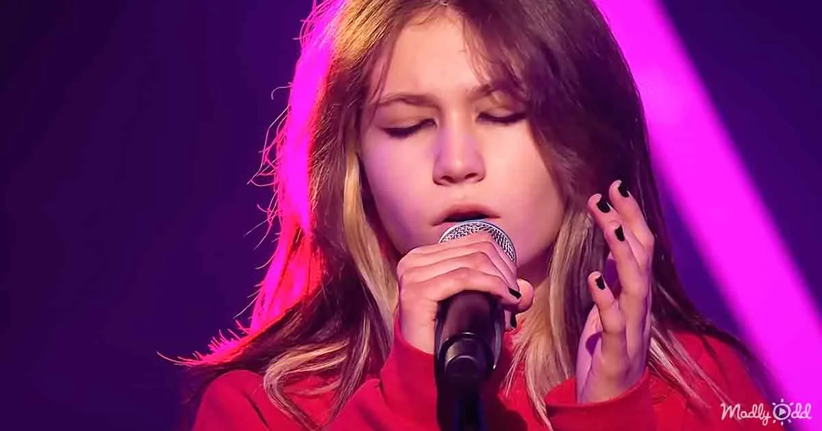 A person in a red shirt sings into a microphone with a purple light behind them.