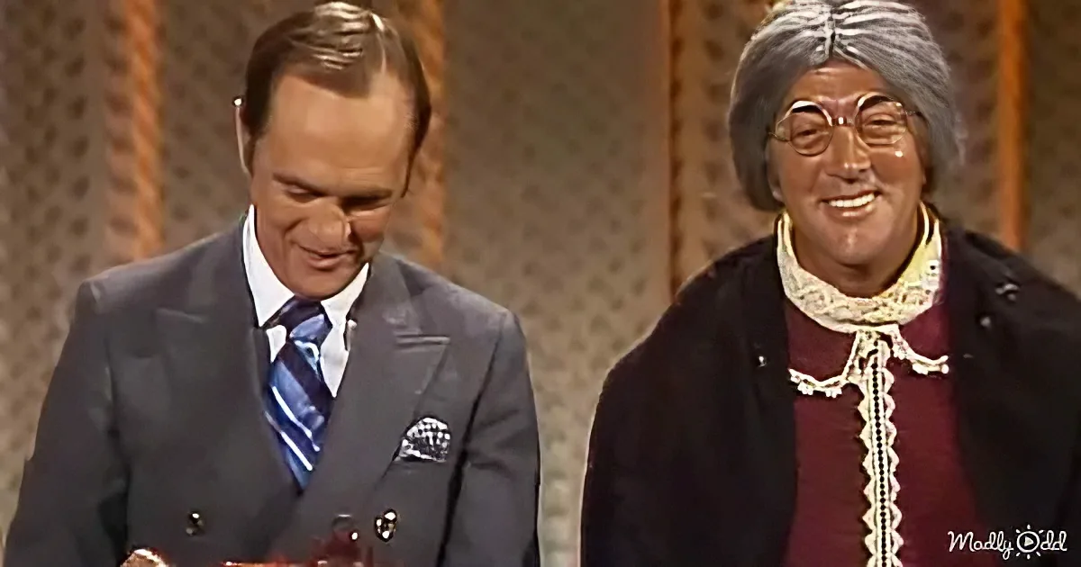 A man in a suit and tie stands beside another man in a costume, both smiling.