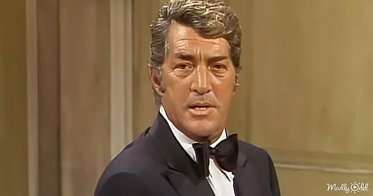 A man in a tuxedo with a bow tie stands indoors, looking slightly to the side.