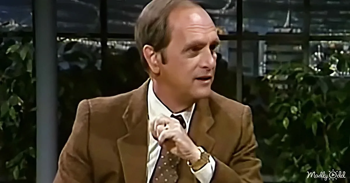 A man in a brown suit and tie is gesturing with his hands while speaking.