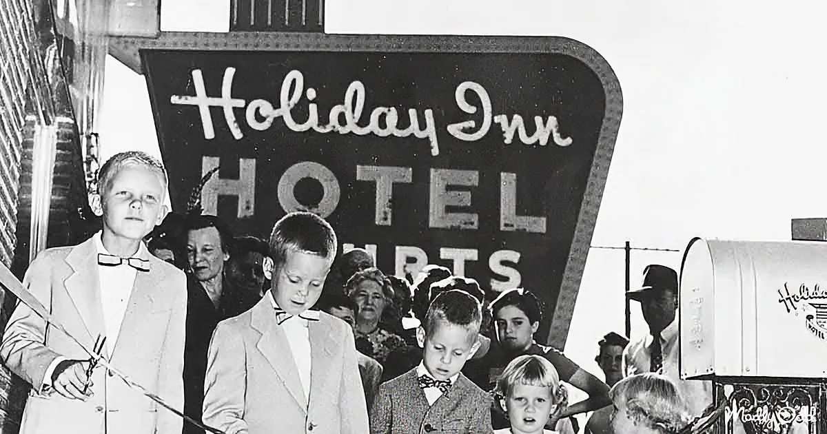 Children in suits stand in front of a "Holiday Inn" sign, cutting a ribbon at an opening ceremony.