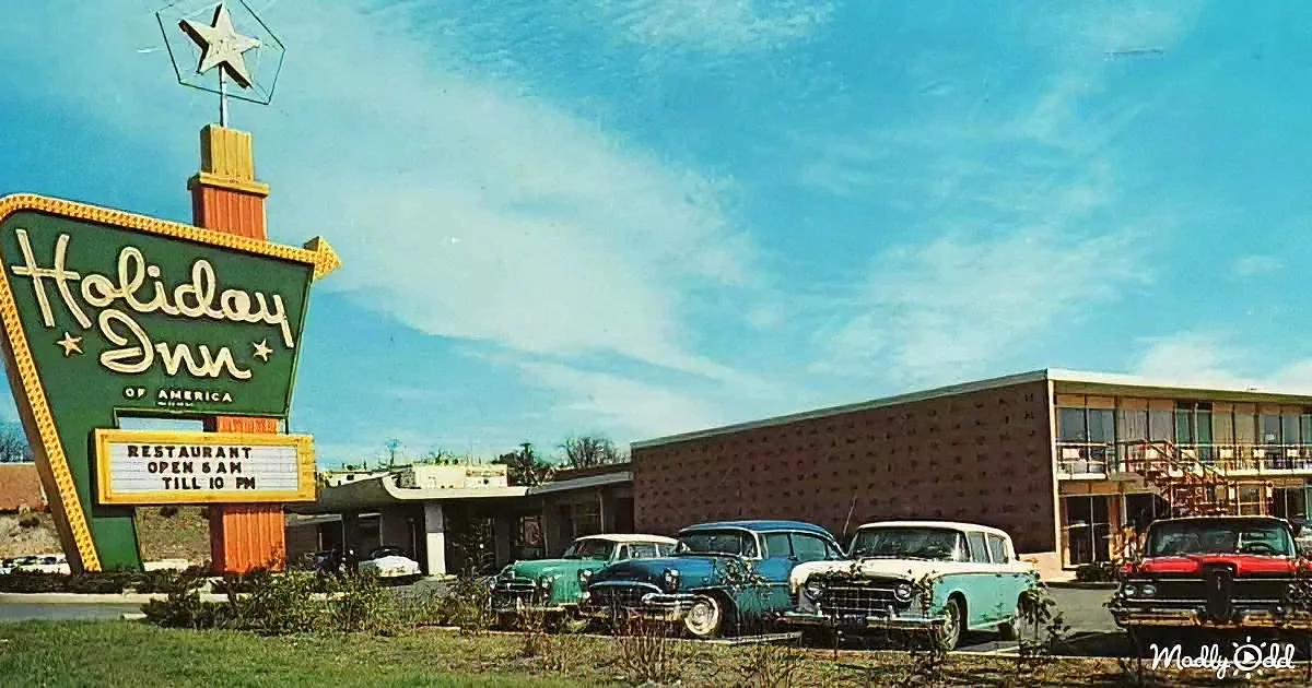 Holiday Inn sign with vintage cars parked in front, clear blue sky, retro motel building.