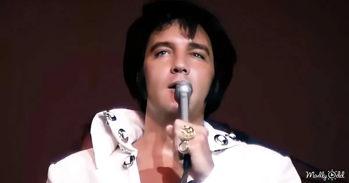 Elvis Presley in a white outfit singing into a microphone.