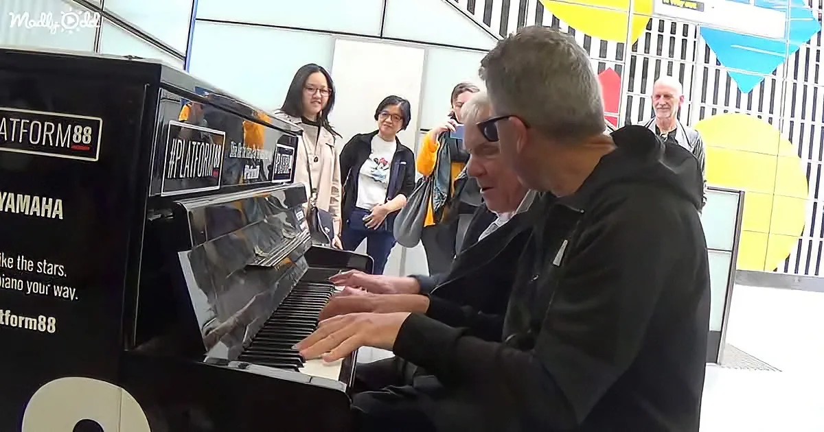 A man plays a black Yamaha piano in a public space, surrounded by onlookers.