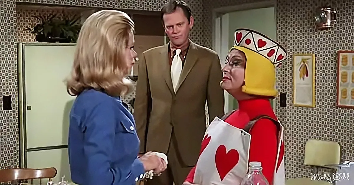 A woman in a blue suit shakes hands with a person in a red and yellow costume in a retro kitchen.