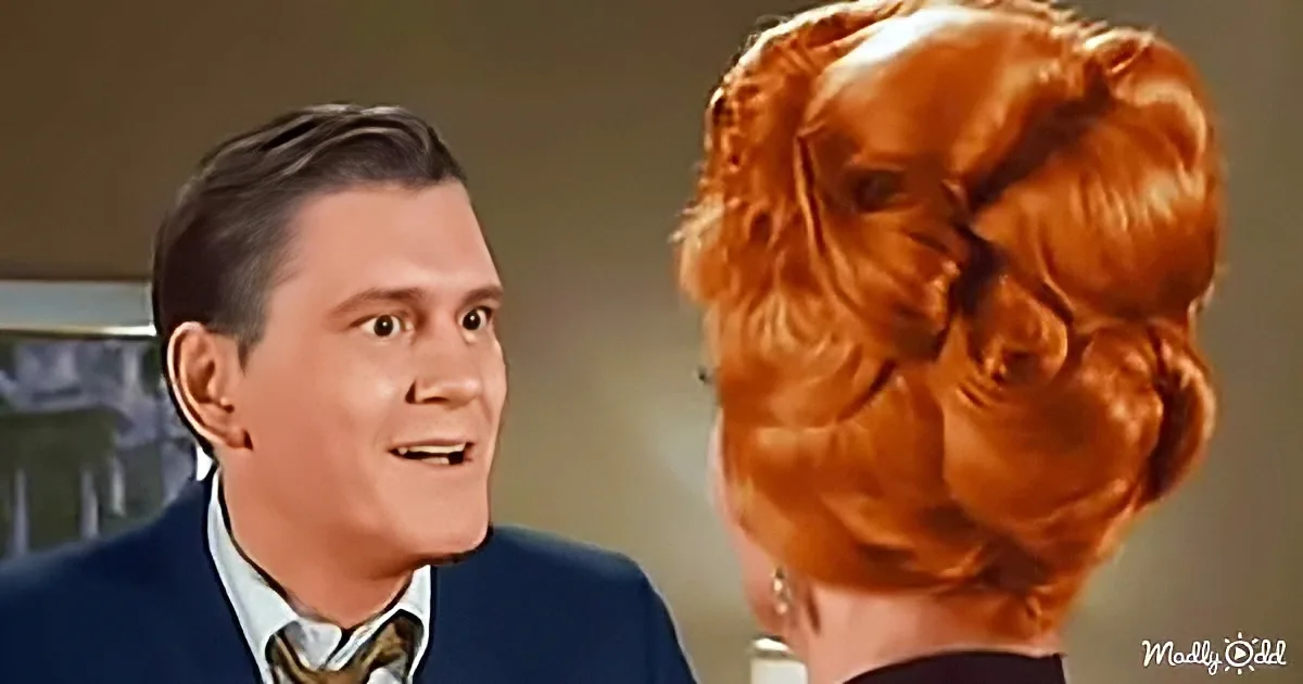 A man in a suit and bow tie smiles at a woman with voluminous red hair in a bun.
