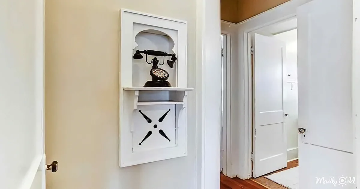 A vintage telephone is displayed on a white shelf in a hallway.