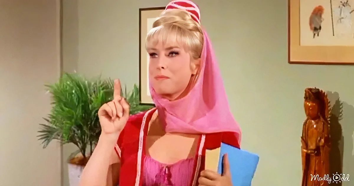 A woman in a pink and red outfit with a pink headscarf points upwards while holding a blue folder.