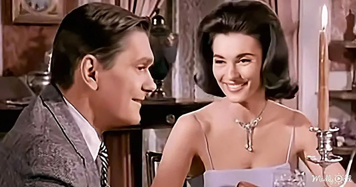 A man and woman smile at each other in a warmly lit, vintage setting, suggesting a romantic or intimate moment.
