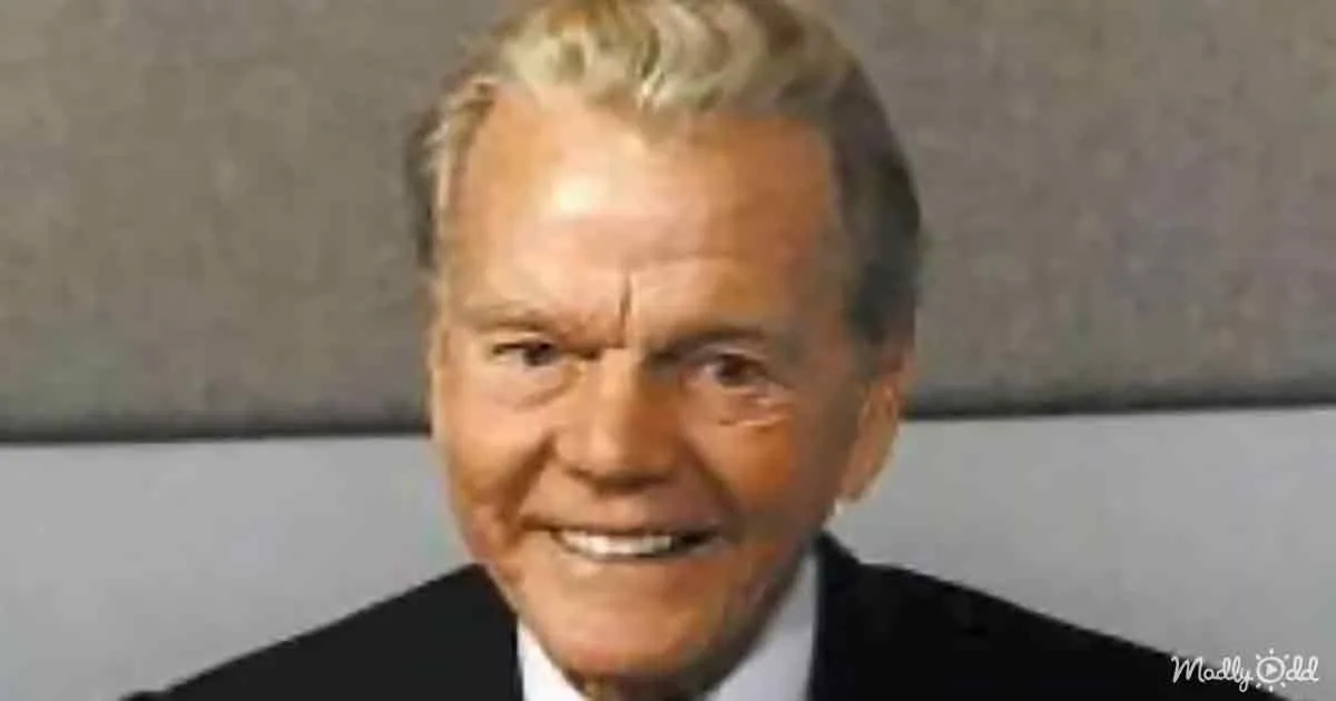 A smiling man with light-colored hair, wearing a dark suit and white shirt.