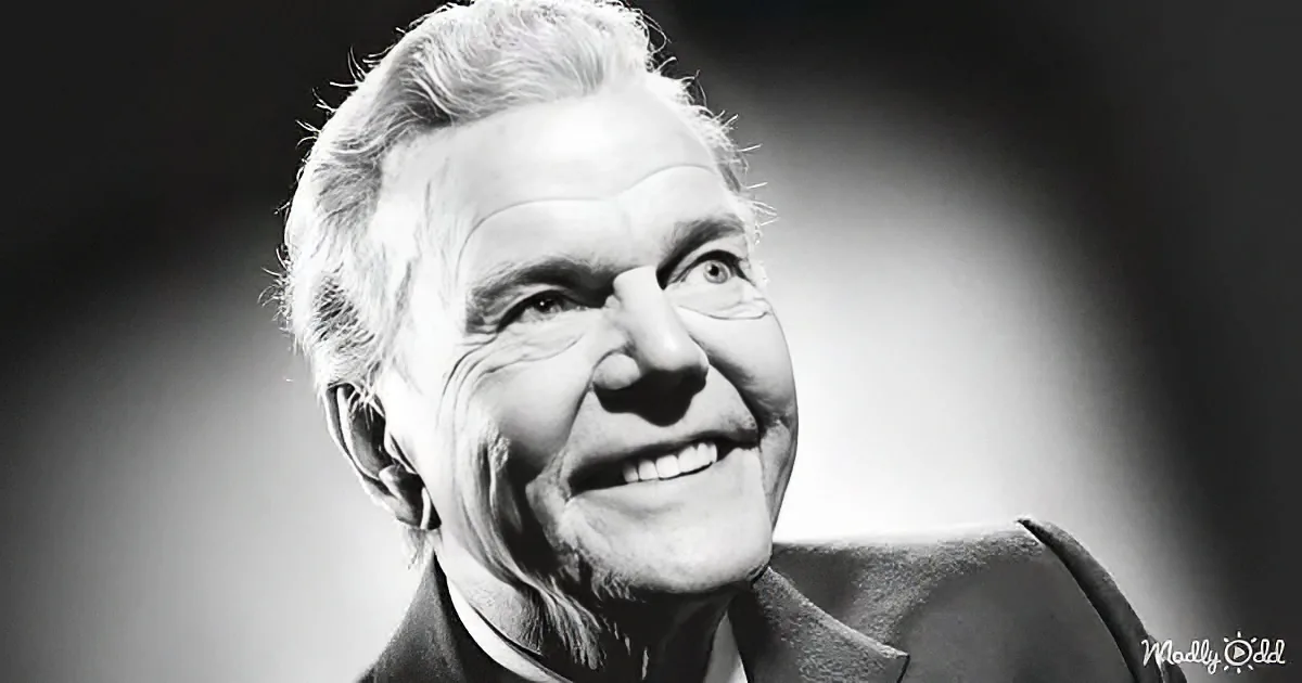 A smiling older man with white hair, wearing a suit, against a dark background.