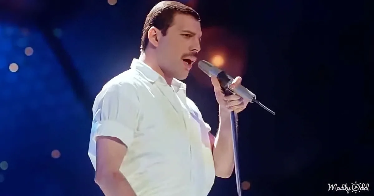A man in a white shirt sings passionately into a microphone on stage.