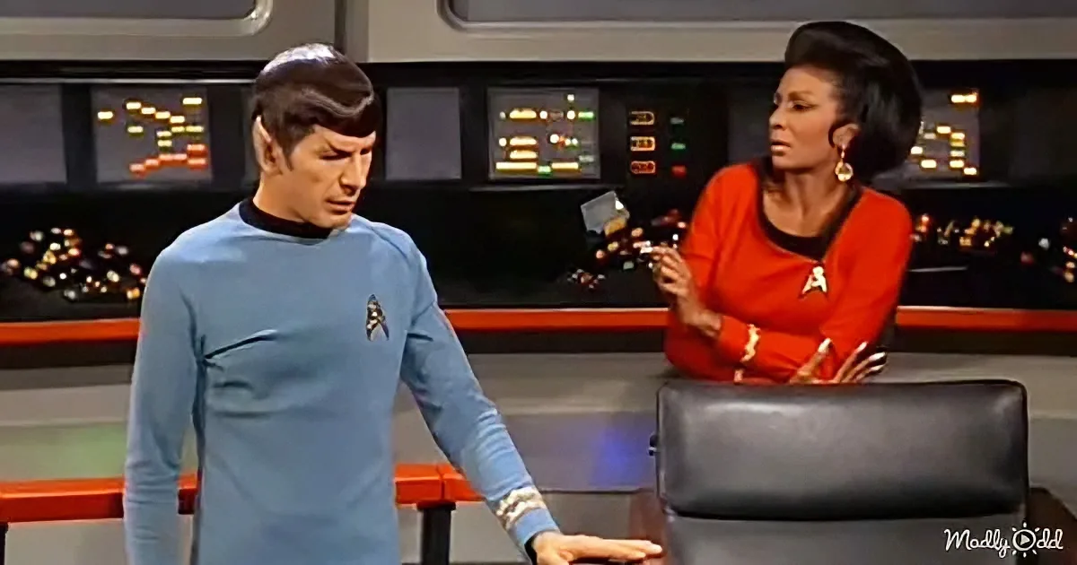 Spock and Uhura in a Star Trek scene, Spock looking down, Uhura gesturing, in a control room.