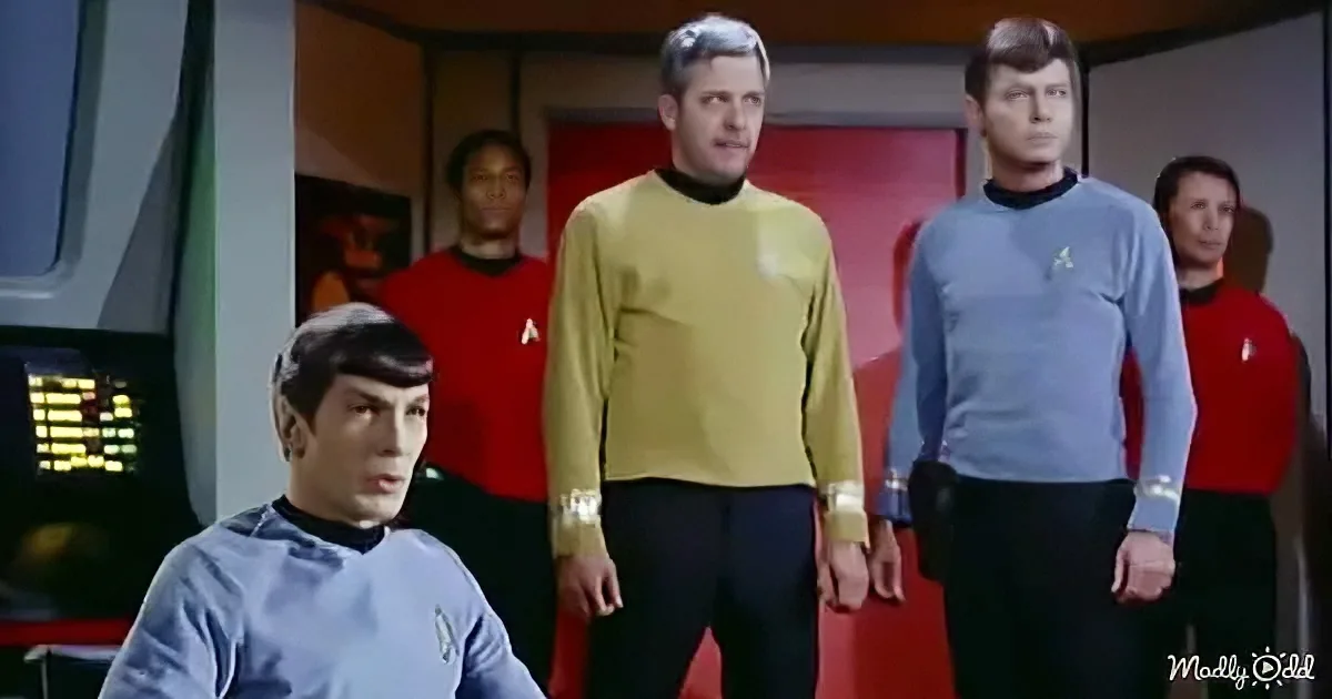 A Star Trek character in a blue uniform sits in front of a group of crew members in red and yellow uniforms.