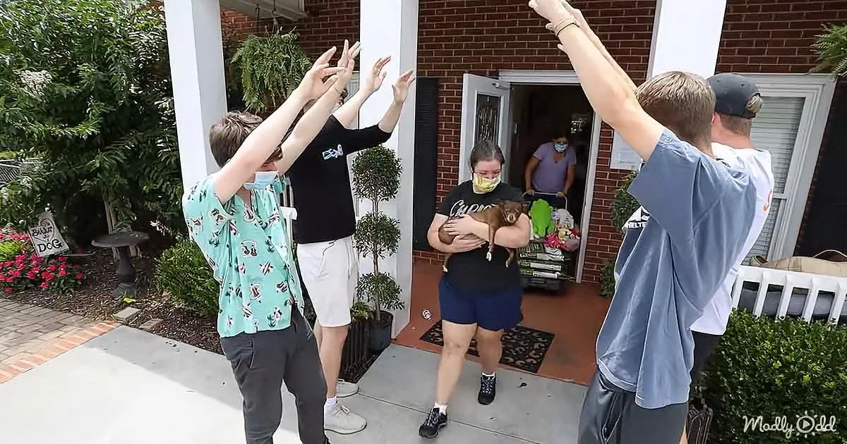 A group of people, some in masks, raise their arms in celebration outside a house.