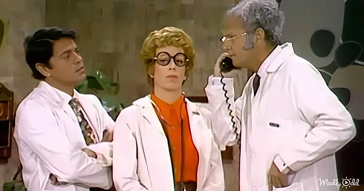 A man in a lab coat talks on the phone while two others, also in lab coats, listen and observe.