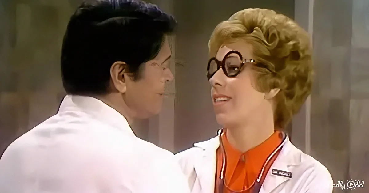 A person in a lab coat and orange shirt is facing another person in a white lab coat.