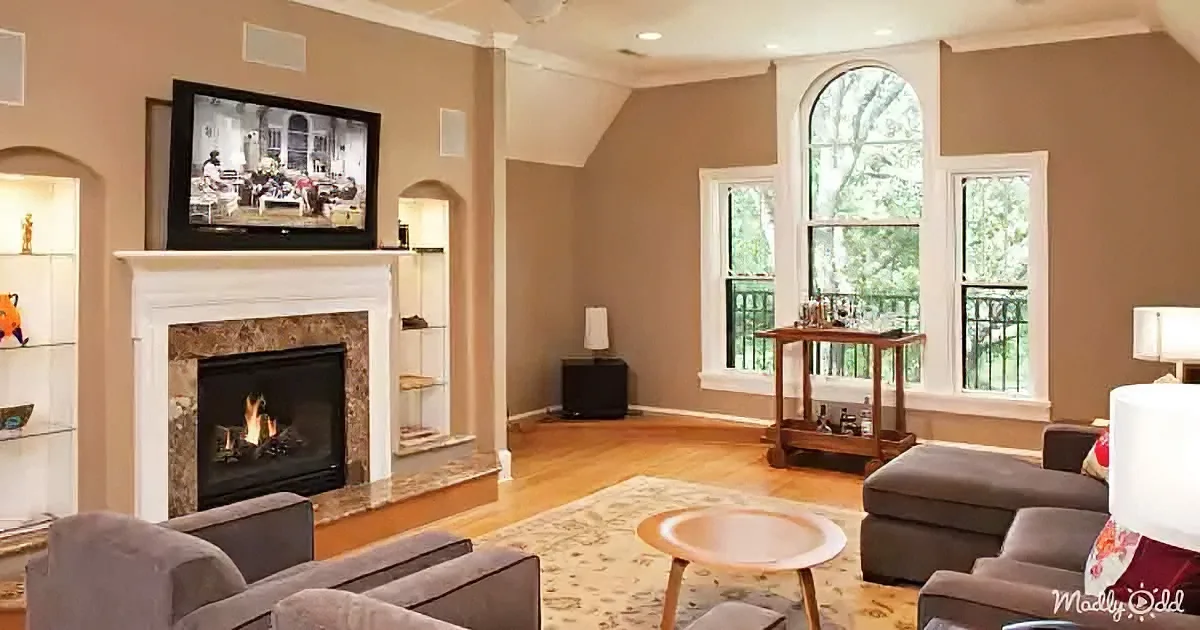 A cozy living room with a fireplace, TV, and large windows letting in natural light.