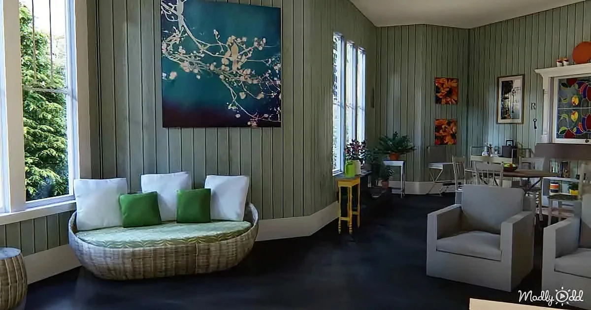 A cozy living room with a wicker daybed, green and white cushions, and a large floral painting on the wall.