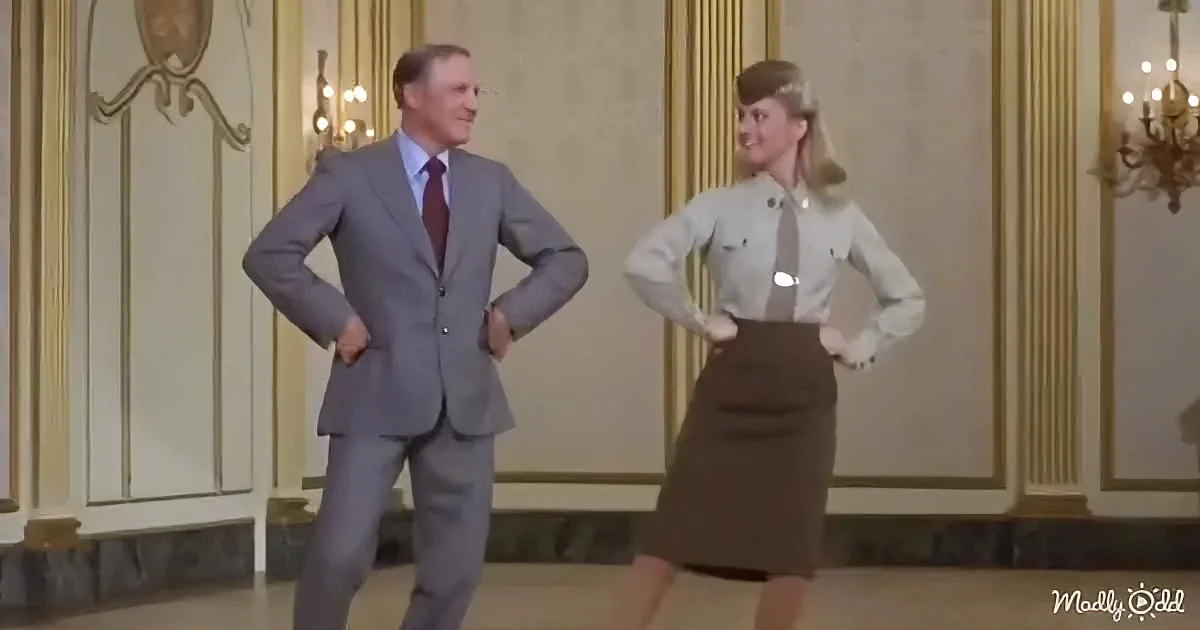 A man in a suit and a woman in a uniform pose confidently in a grand room.