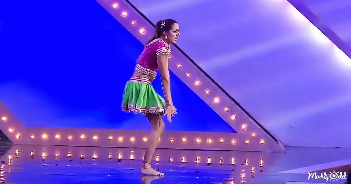 A woman in a colorful outfit stands on a stage with a blue and purple backdrop and illuminated lights.