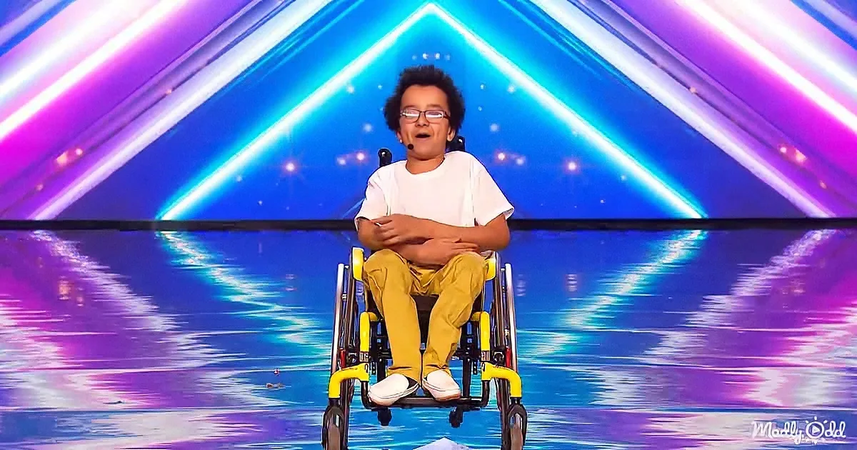 A young person in a wheelchair smiles on a stage with vibrant purple and blue lighting.