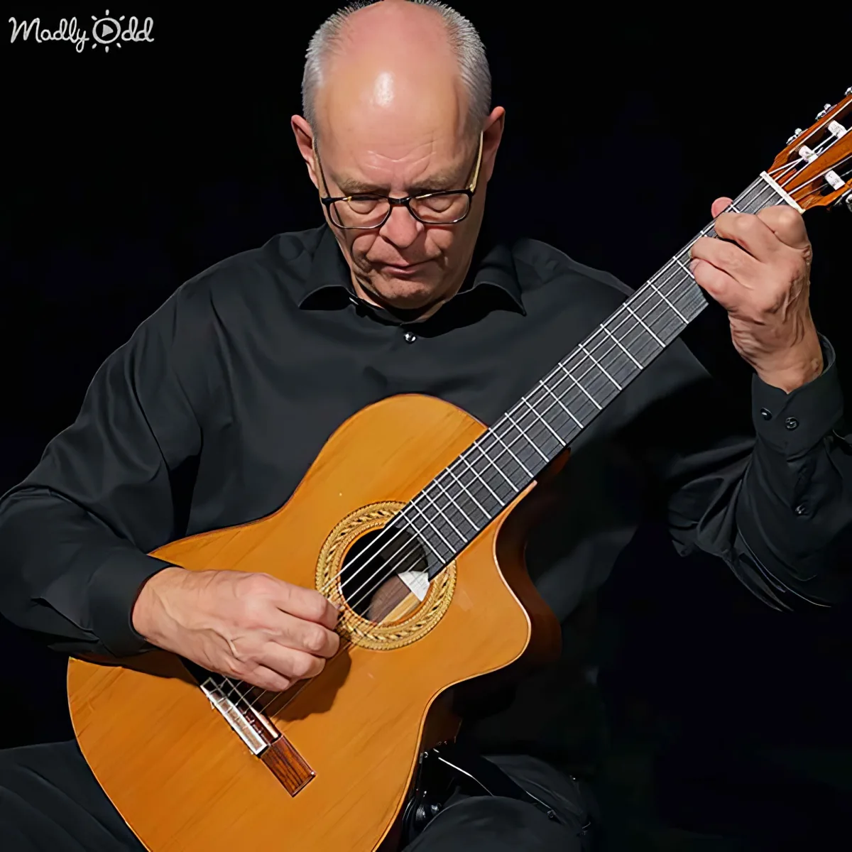 A man in black plays a classical guitar with focused concentration.