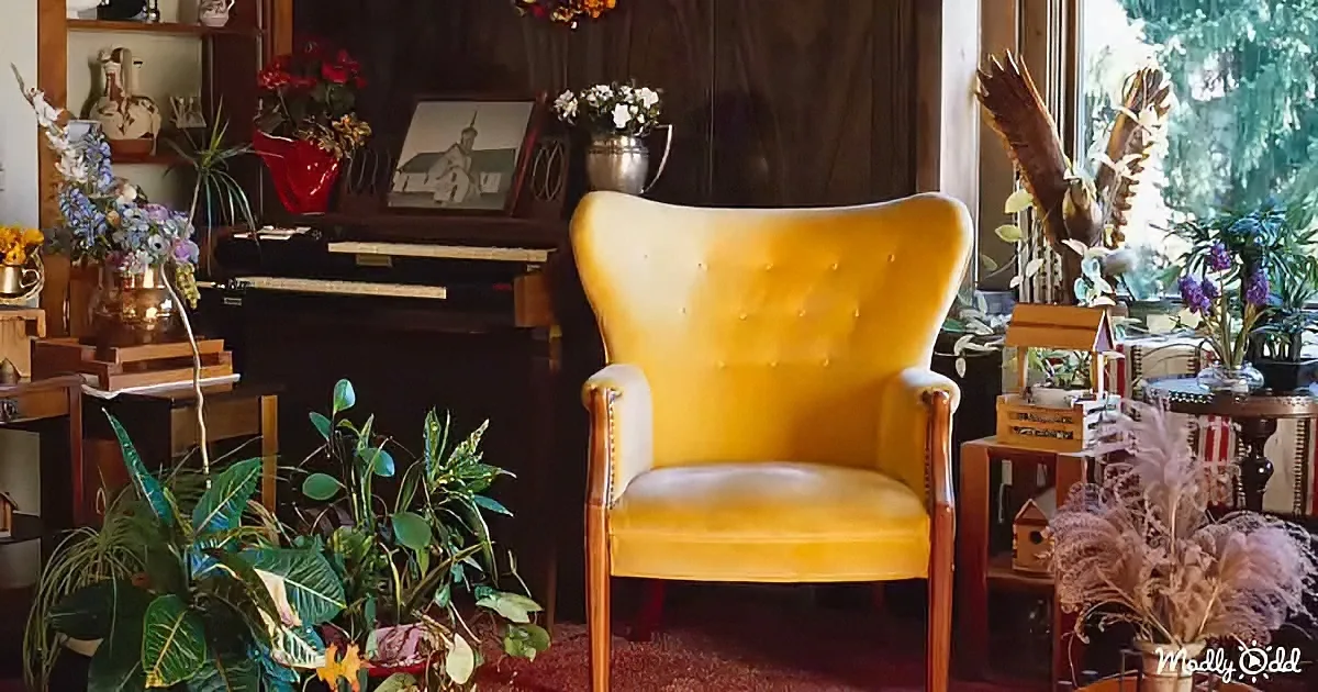 A mustard-yellow wingback chair sits in a cozy room filled with plants, flowers, and vintage decor.