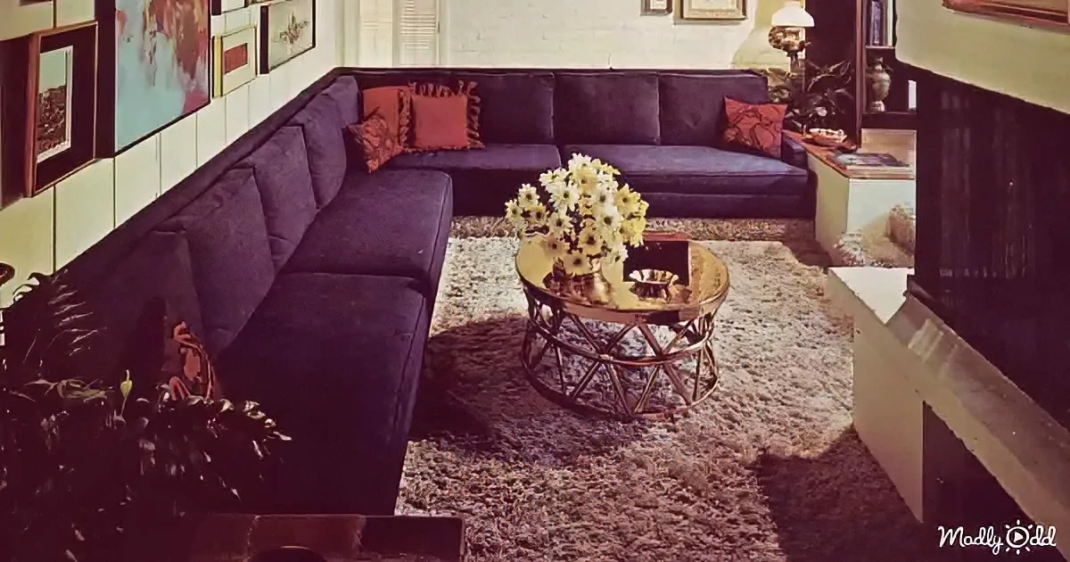 A retro living room features a large purple sectional sofa, a shaggy rug, and a gold-framed coffee table with flowers.