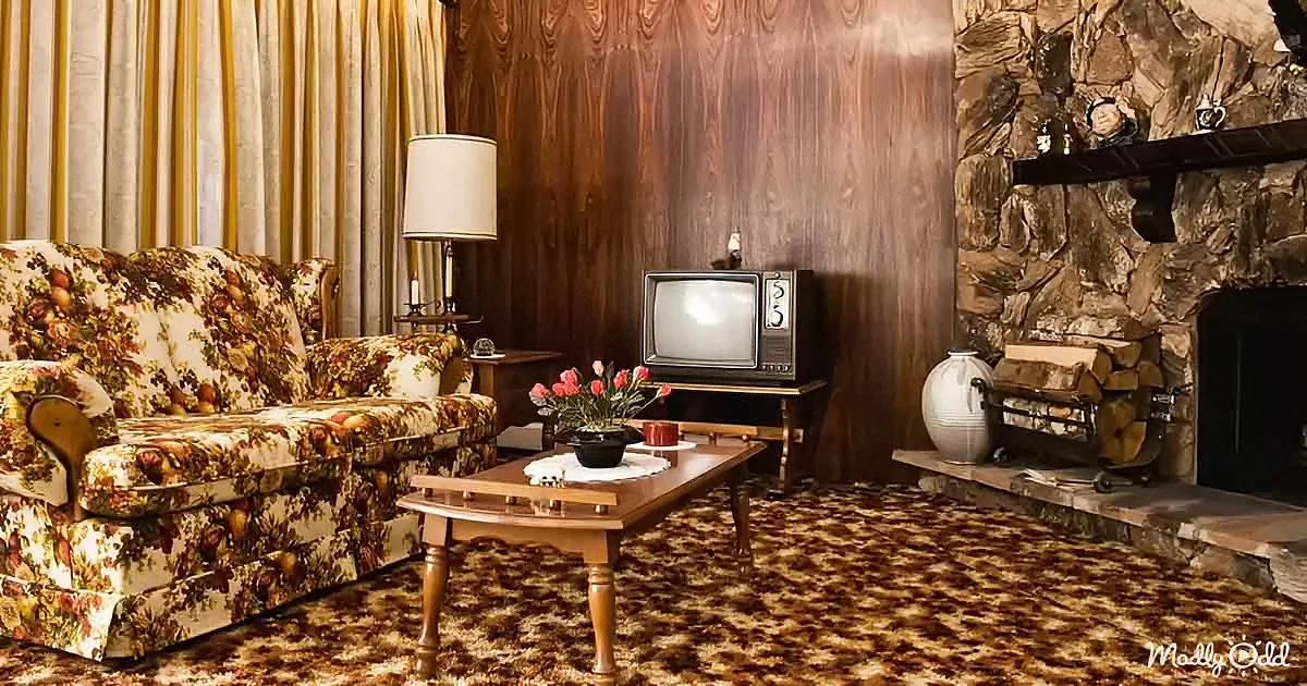 Vintage floral couch, wood-paneled wall, stone fireplace, retro TV, patterned carpet, and classic decor.