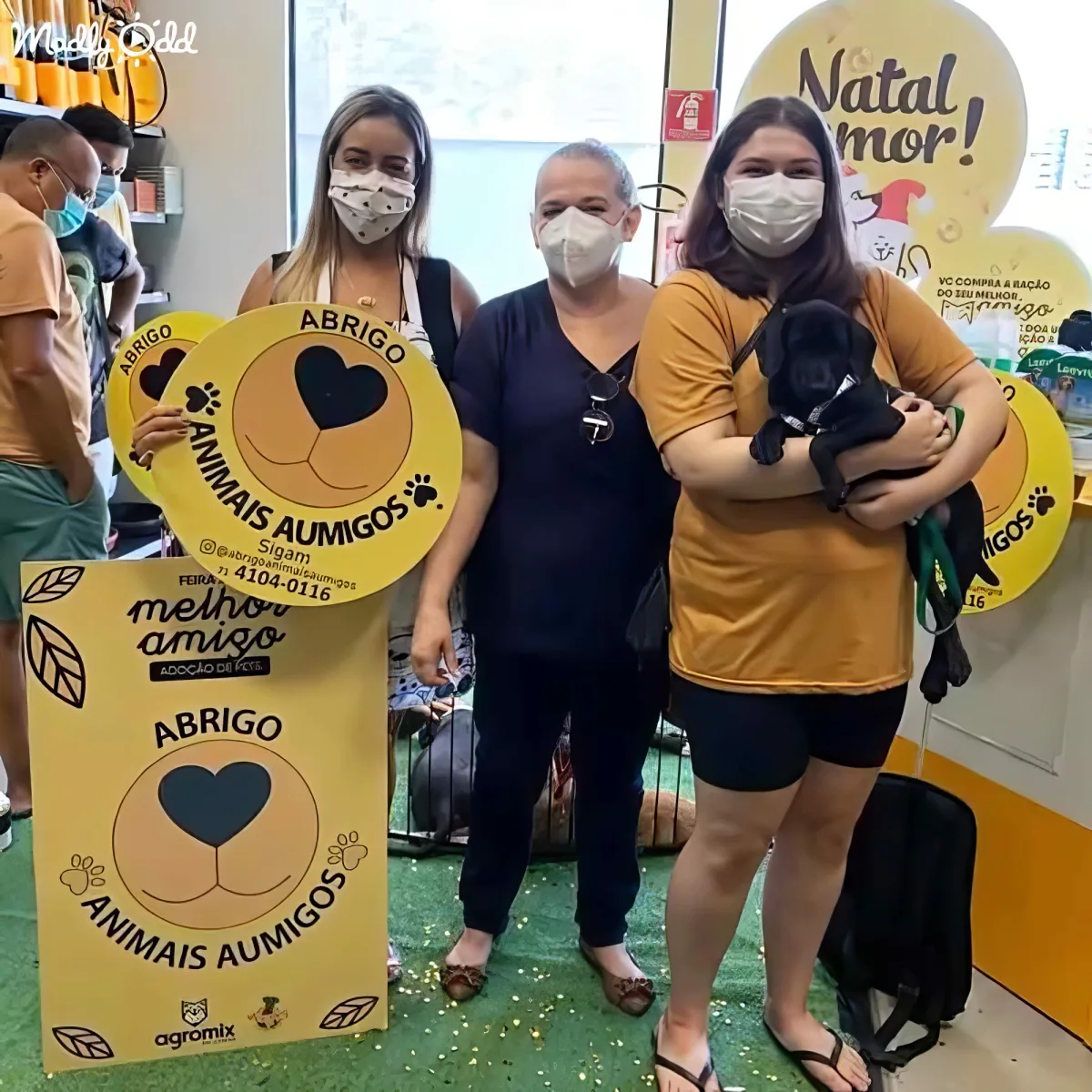A woman holds a black puppy while standing with others at an animal shelter event.