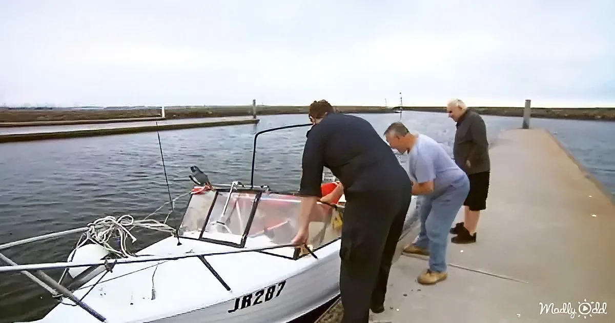 Three men assist a boat into a docked position near calm water.