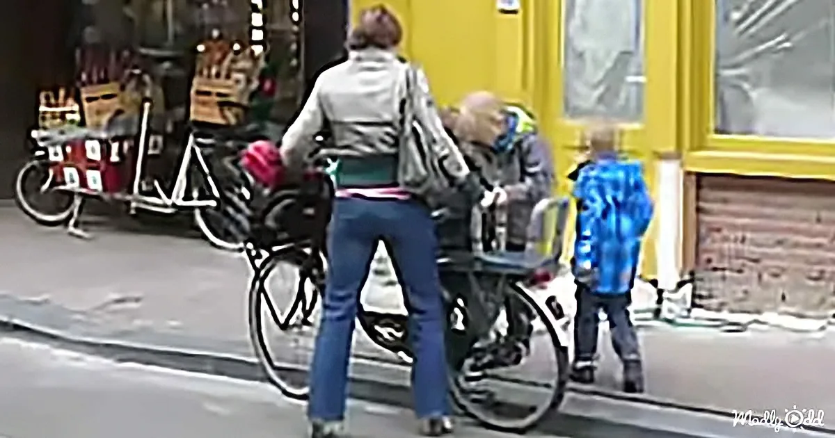 A woman walks past a man and a child on a sidewalk with bicycles and a cart nearby.