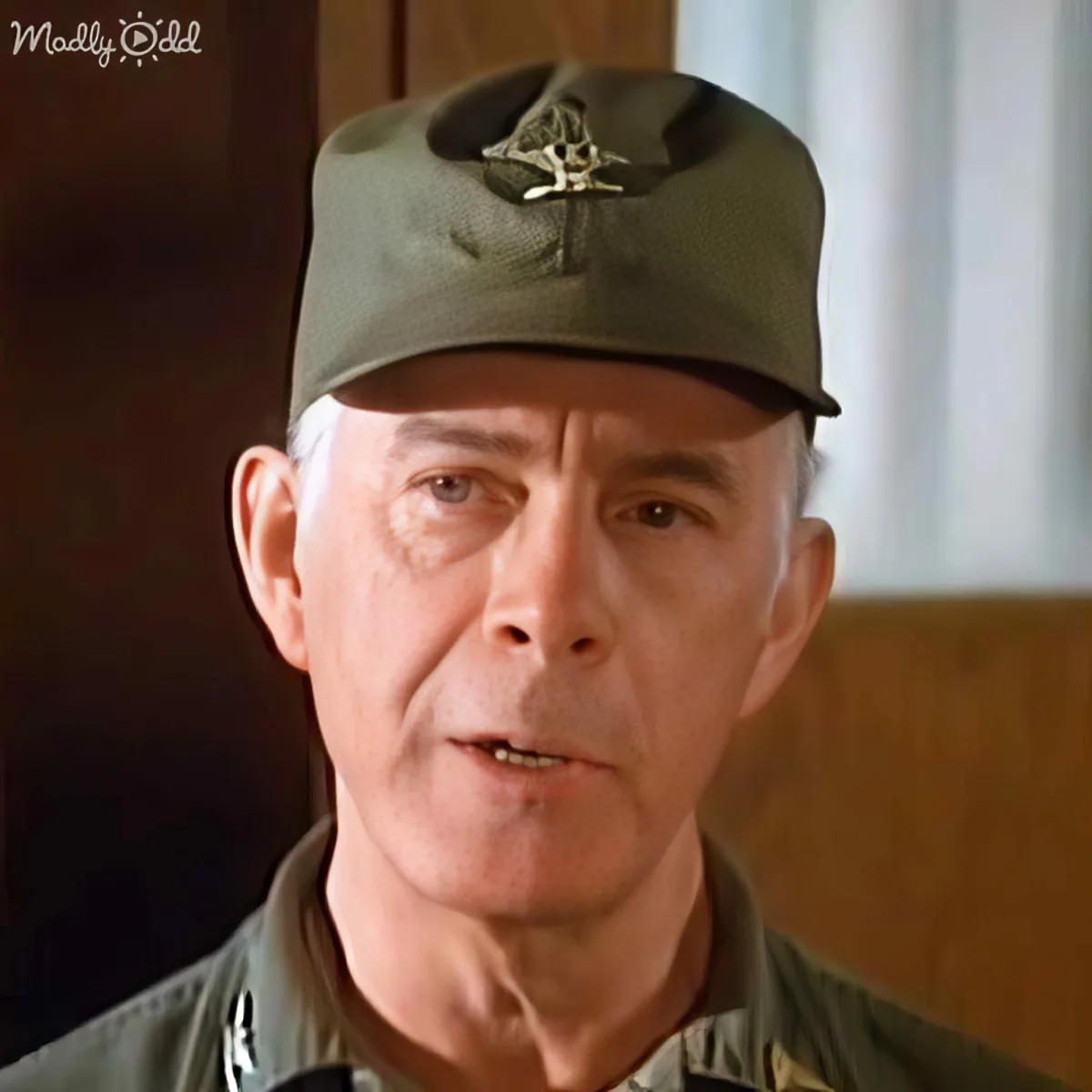 An older man in a military uniform and cap is speaking, with a blurred background.