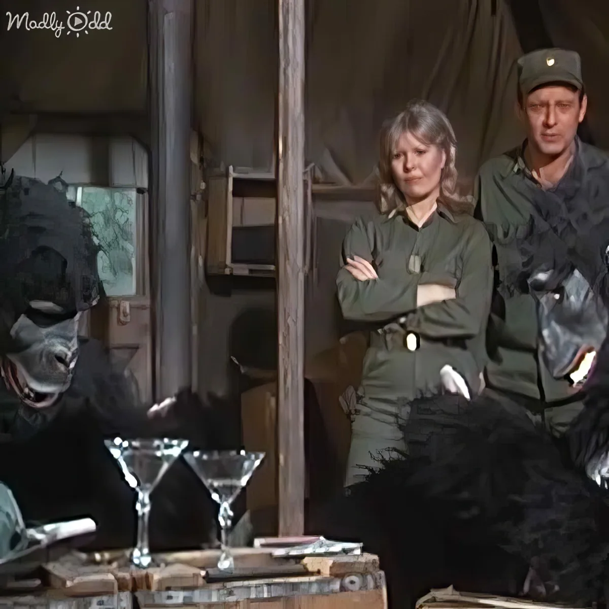 A person in a gorilla suit interacts with two individuals in military attire in a tent setting.