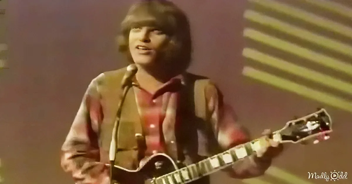 A person in a plaid shirt plays a guitar on stage with a microphone in front of them.