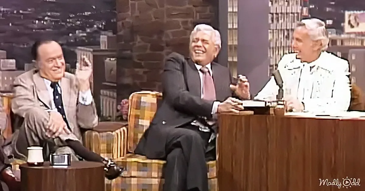Three men in a studio setting, one gesturing, another laughing, and the third smiling, with a cityscape backdrop.