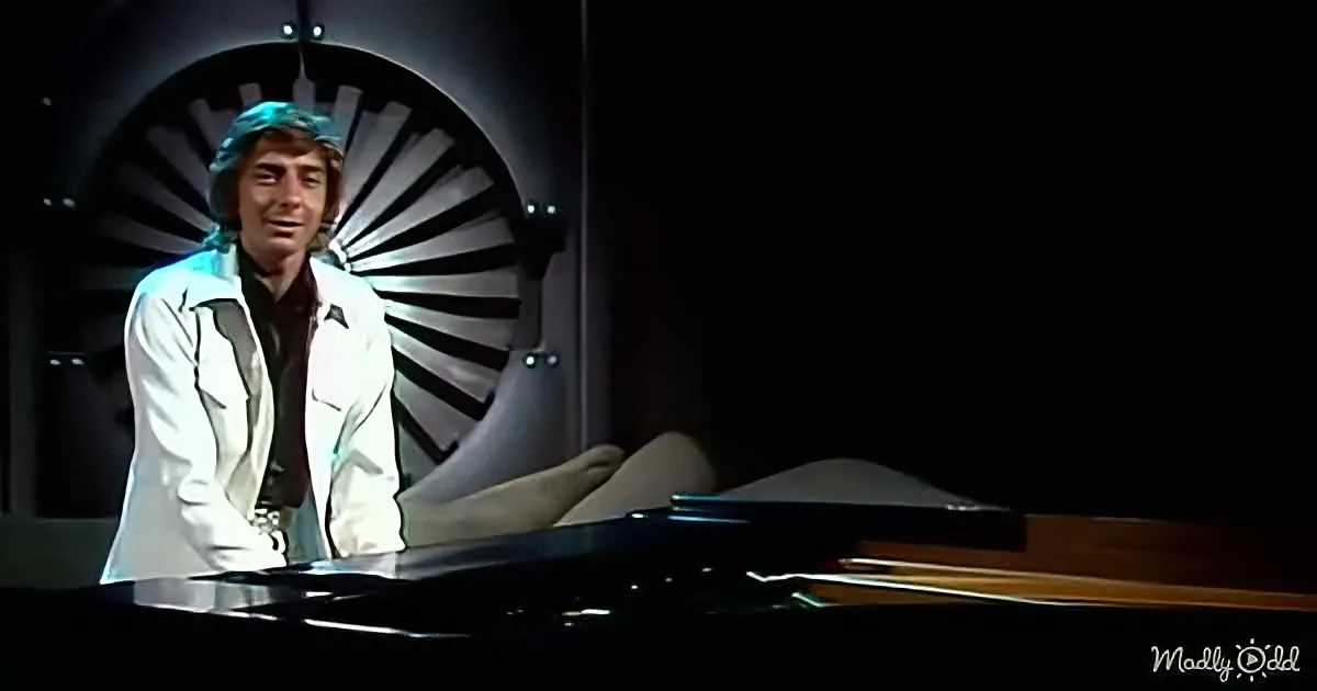 A man in a white jacket stands behind a piano, with a futuristic, circular background.