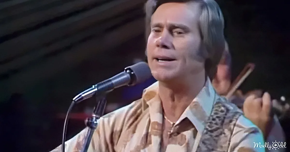 A man in a patterned shirt sings into a microphone, with a guitarist in the background.