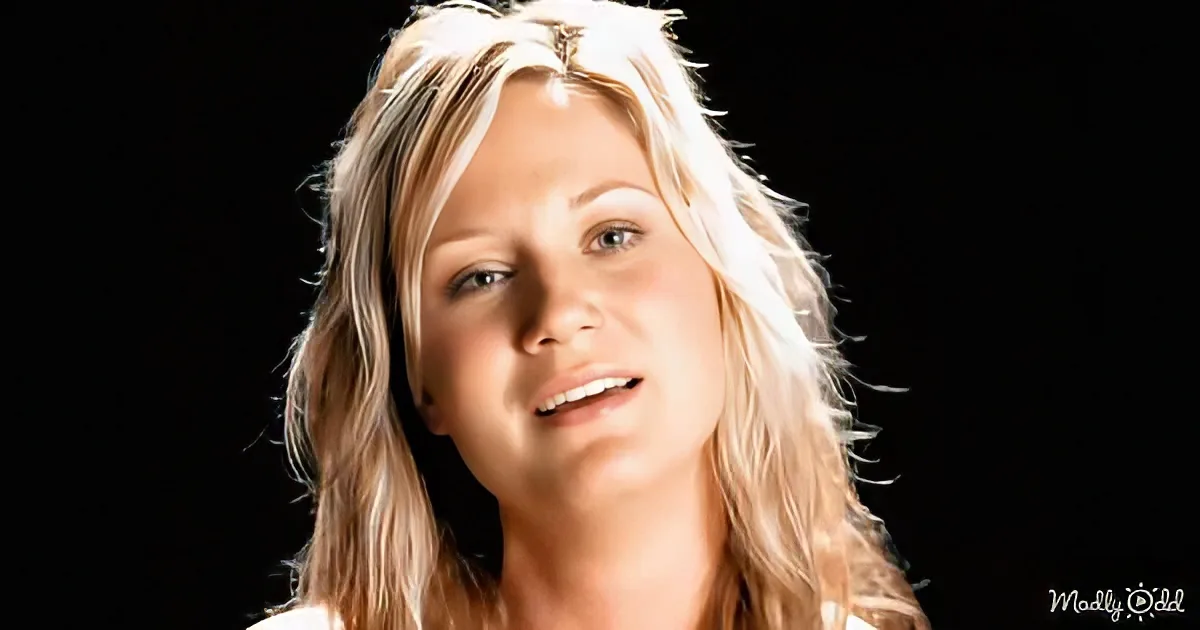 A woman with blonde hair and a black background, looking upwards with a slight smile.